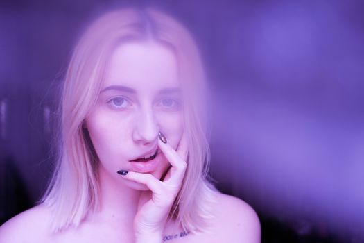 Attractive young woman with blond hair and nail manicure pulling top lip while looking at camera with smoke effect