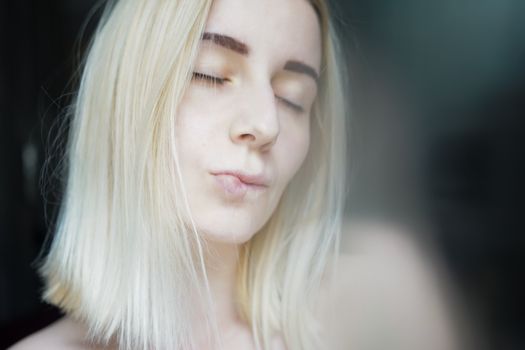 Crop pretty young woman with blond hair and dark eyebrows delicately pursing lips