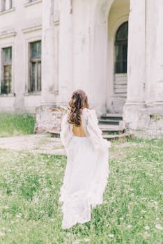 一名身穿白色飘逸连衣裙的女子，走向一栋绿树成荫的复古建筑