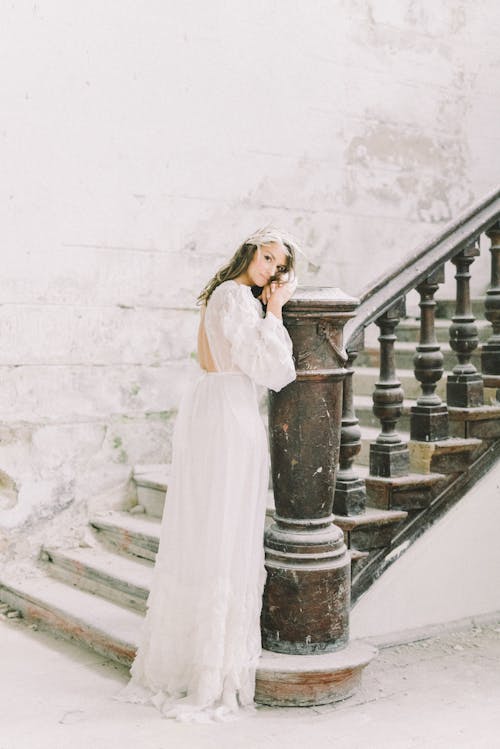 Back view of elegant lady in long bridal dress leaning on column of classic stairway in calm snowfall