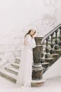 Back view of elegant lady in long bridal dress leaning on column of classic stairway in calm snowfall