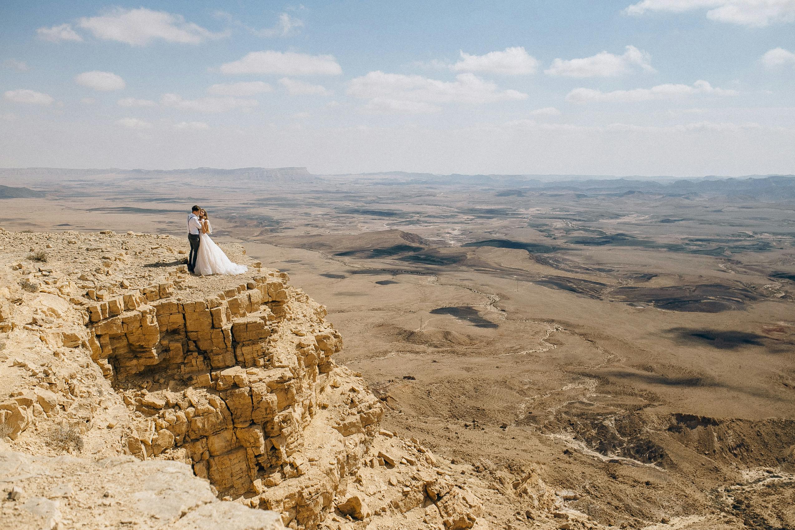 A captivating wedding couple standing on a cliff in a vast desert landscape.