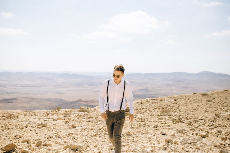 Man In White Long Sleeve Polo And Pants Standing On Rocky Sand