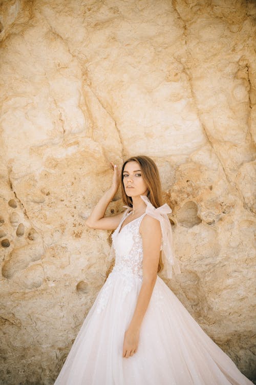 A Woman in Wedding Dress Standing Beside Brown Rock Formation