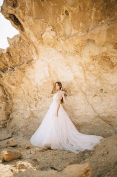 一名身穿婚纱的女子在明亮的阳光下，对着崎岖的岩石摆姿势