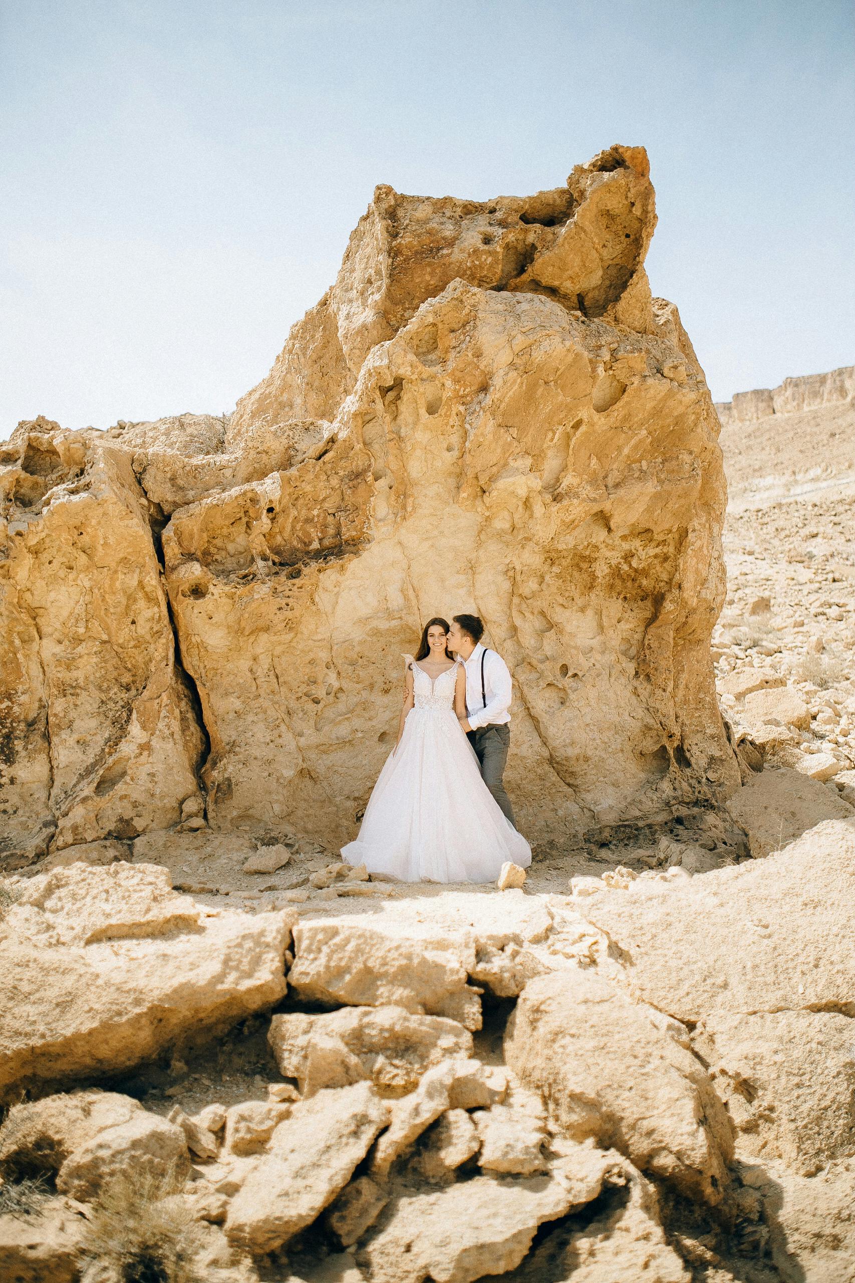 bride and groom standing beside a rock formation