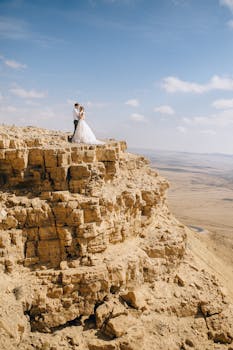 Bride and groom stand together on a rocky desert cliff against a breathtaking landscape.