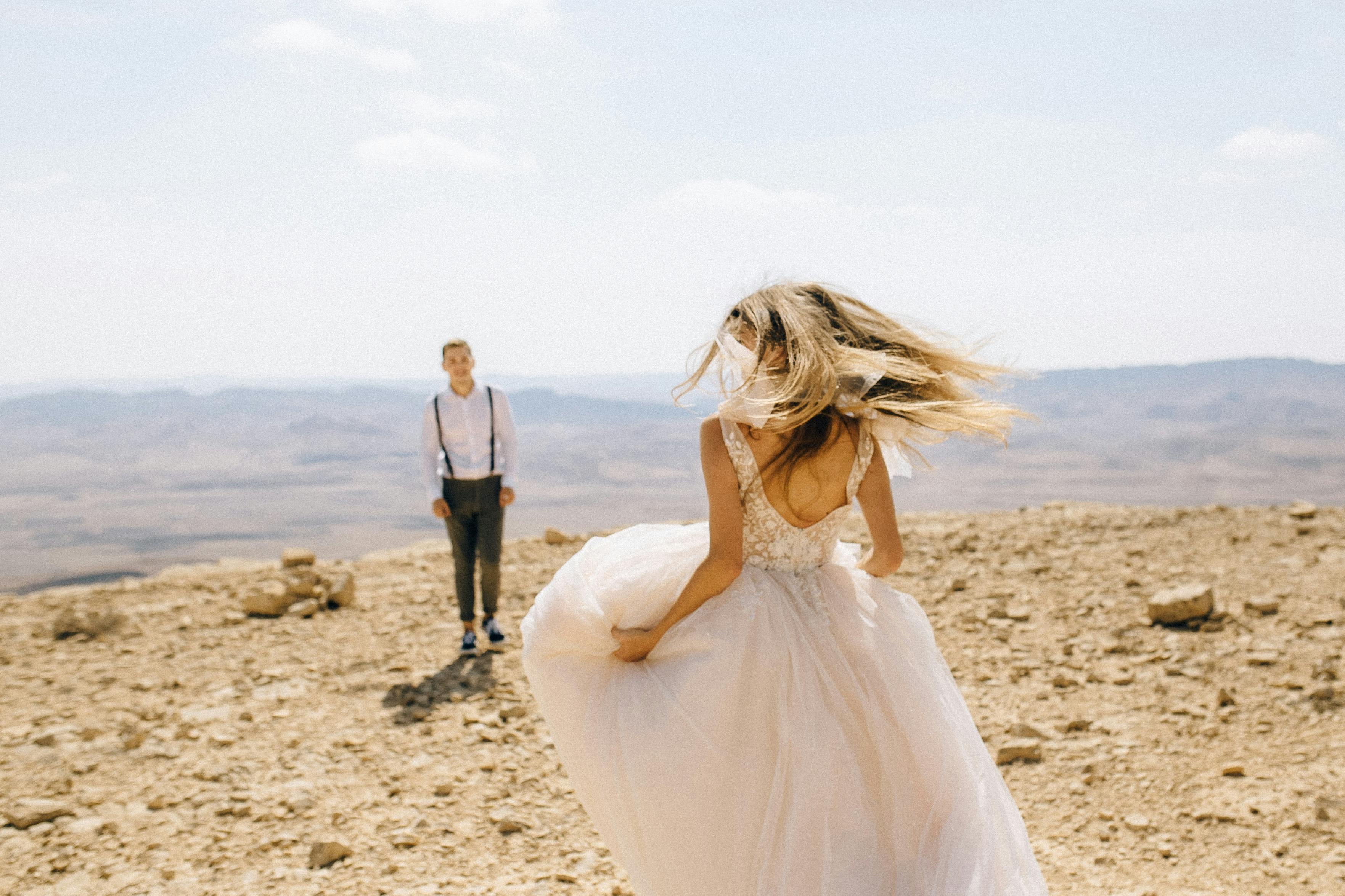Bride in wedding gown runs toward groom in a stunning desert landscape.