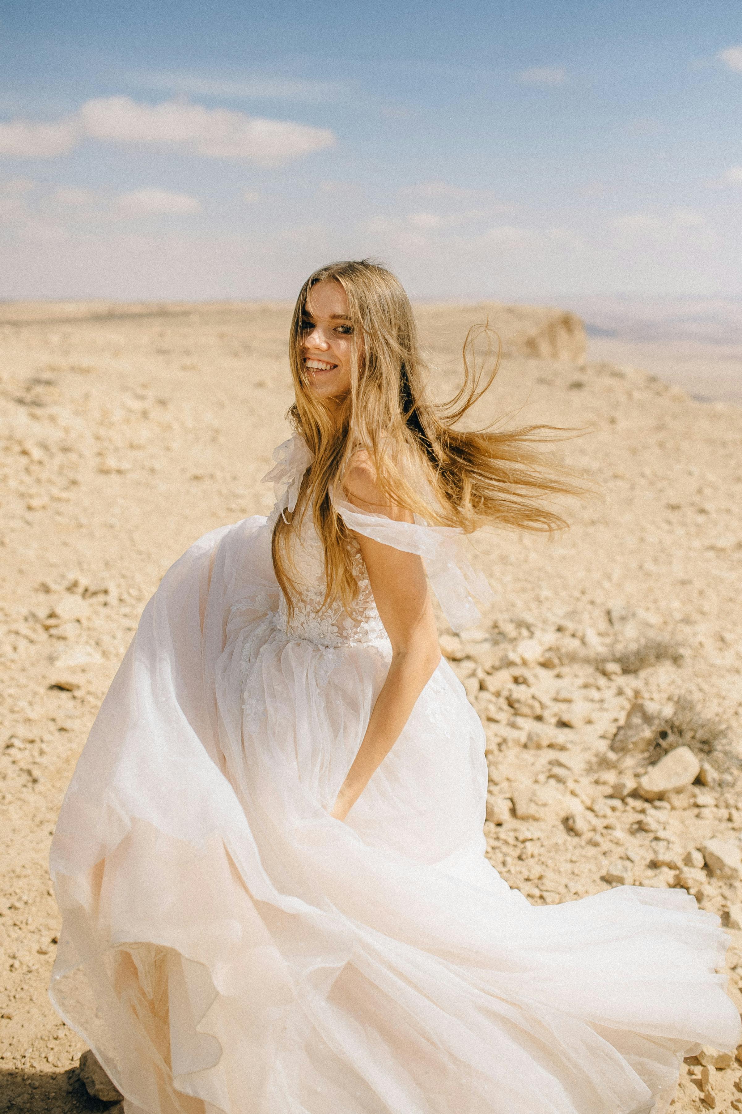 A bride dressed in a flowing wedding gown amidst a vast desert landscape.