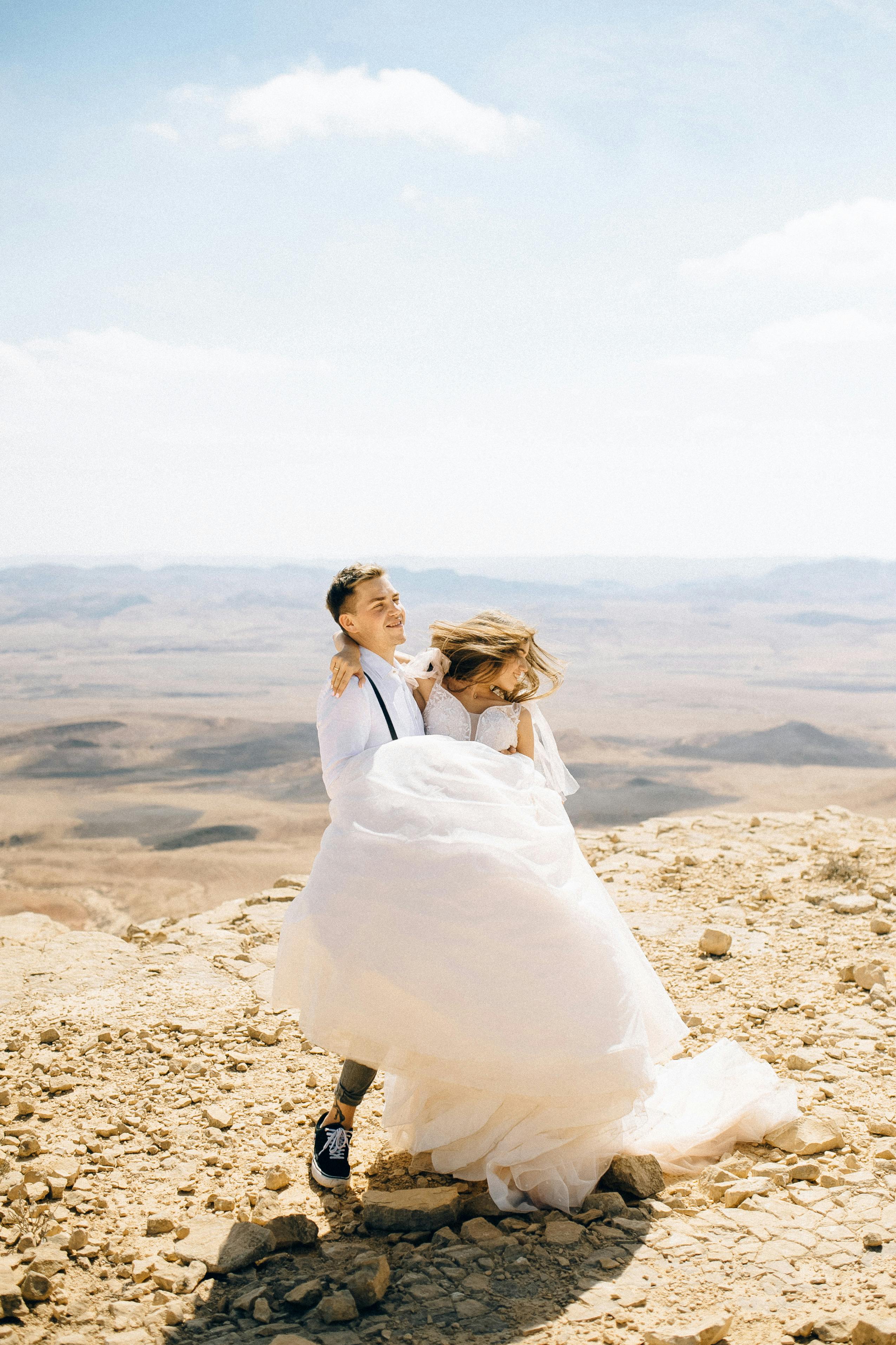 一对夫妇穿着婚纱，在沙漠背景的悬崖上庆祝