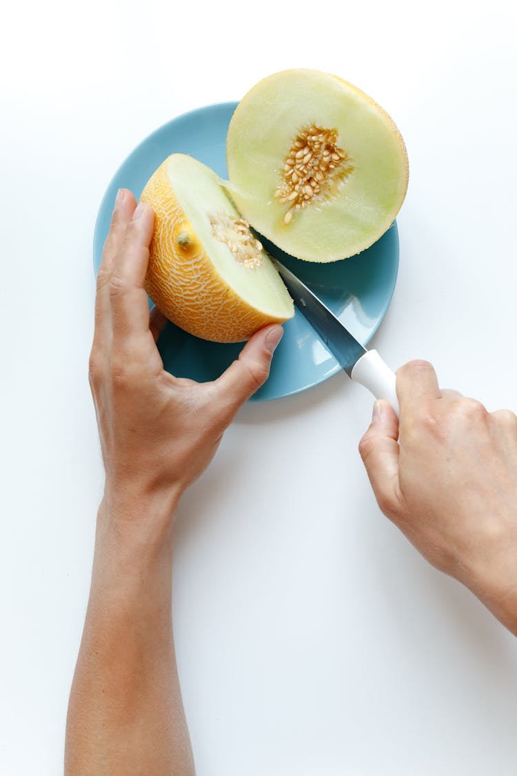 Person Holding Knife Cutting Melon Fruit Into Two