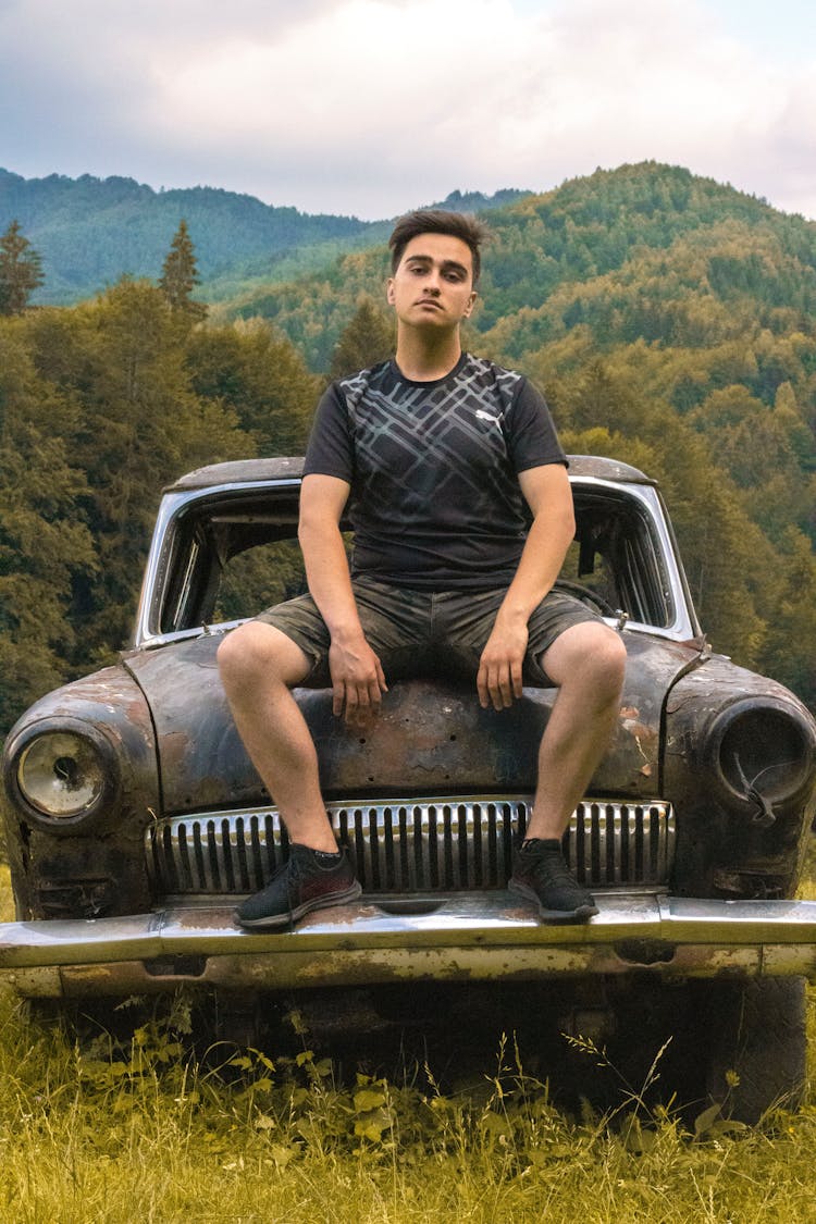 A Man Sitting On Abandoned Car Hood 