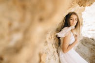 一位身着飘逸白裙的新娘，优雅地倚在质朴的石墙上摆着姿势，显得宁静而美好