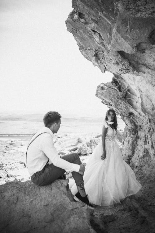 Grayscale Photo of a Couple Sitting on Rock Formation