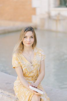 阳光明媚，一位身穿花卉连衣裙的女子，静静地坐在喷泉边