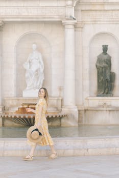 一位穿着黄色连衣裙、戴着帽子的妇女走过一座历史悠久的喷泉