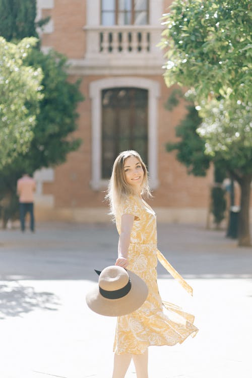 Free Pretty Smiling Woman in Yellow Dress Holding Her Sun Hat Stock Photo