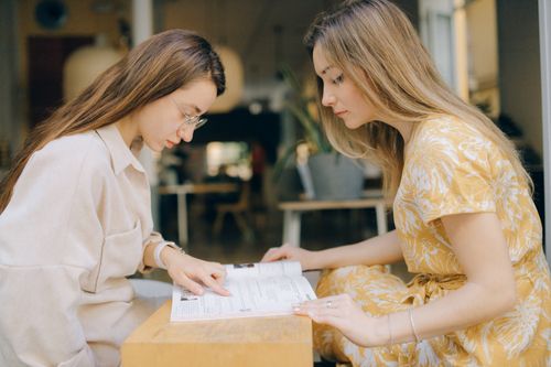 Free Two young women studying together, focusing on a book in a relaxed indoor setting. Stock Photo