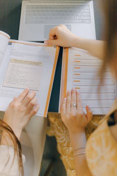 Two people studying together with open books and a laptop, focusing on education.