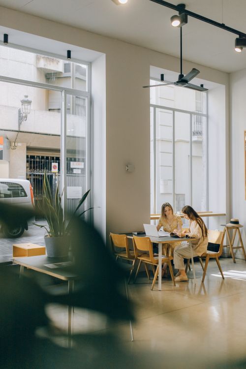 Free Two women engaged in conversation at a bright and stylish coffee shop. Stock Photo