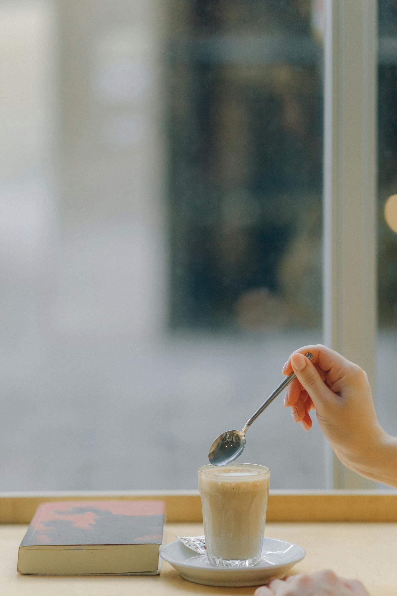 Hand stirring a latte in a glass by a window in a calm morning routine