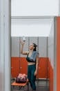 Woman in Blue Leggings Throwing Up Bottle of Water While Standing in the Gym Changing Room