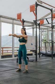 A woman in activewear stretching in a modern indoor gym with a scenic view outside.