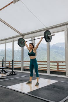 Strong woman weightlifting in an indoor gym with scenic mountain views.