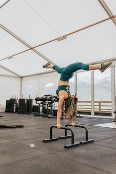 Woman in activewear doing a handstand on gym bars, showcasing strength and balance.