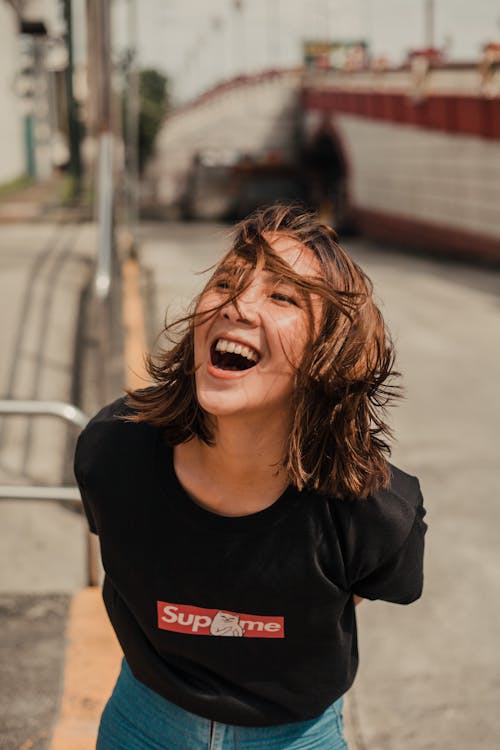 Cheerful young female with short hair and in black t shirt with denim standing near metal fence and laughing