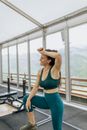 在现代化的室内健身房里，一位穿着运动服的女子微笑着休息，欣赏着美丽的山景