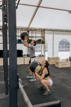 Man and woman performing medicine ball exercises in a gym setting.