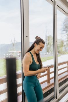 一名穿着运动服的微笑女子在室内玻璃墙附近使用智能手机，捕捉到了一个坦率的瞬间