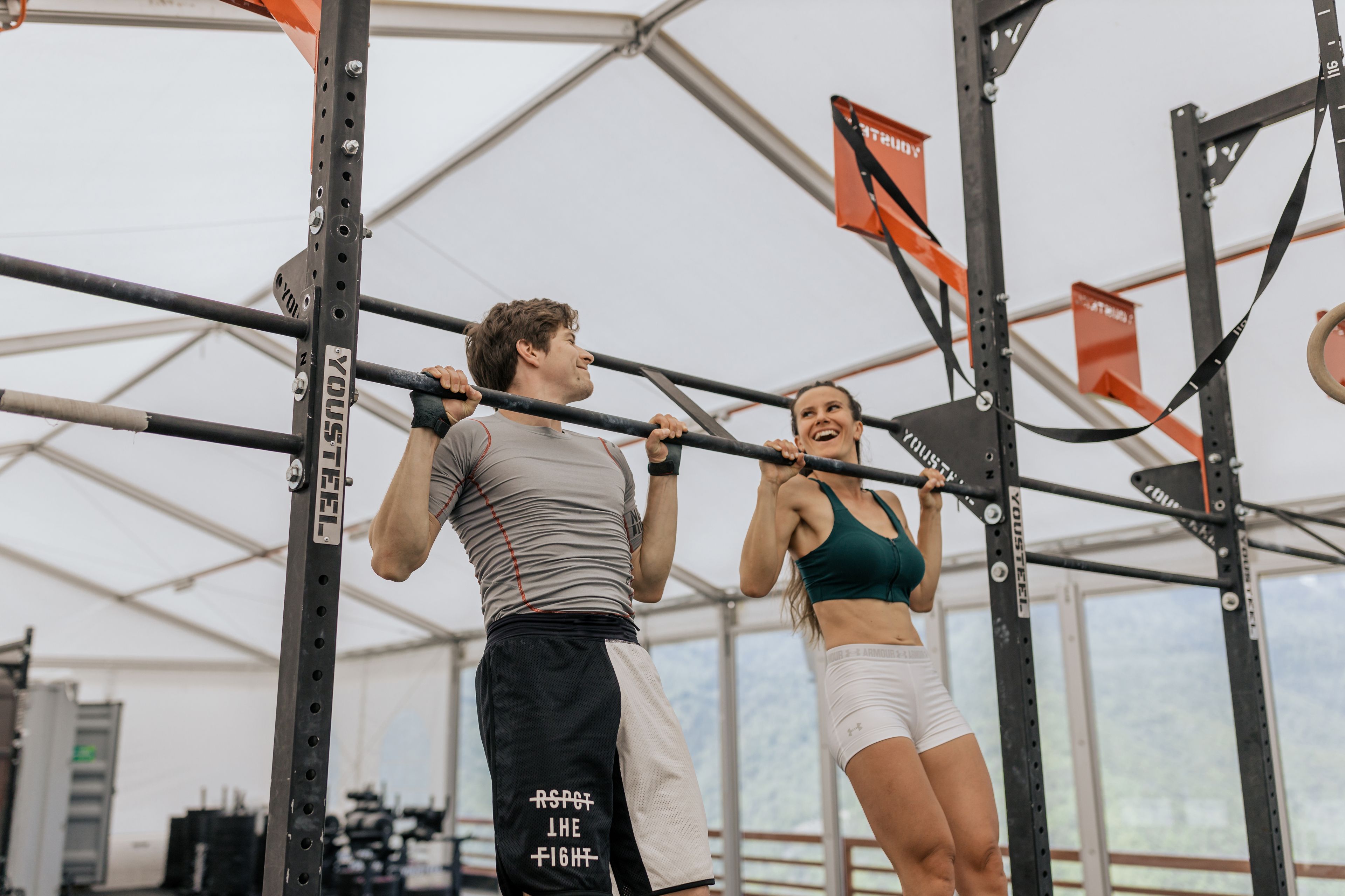 Man and woman exercising with pull-ups in an indoor gym, showcasing fitness and strength.