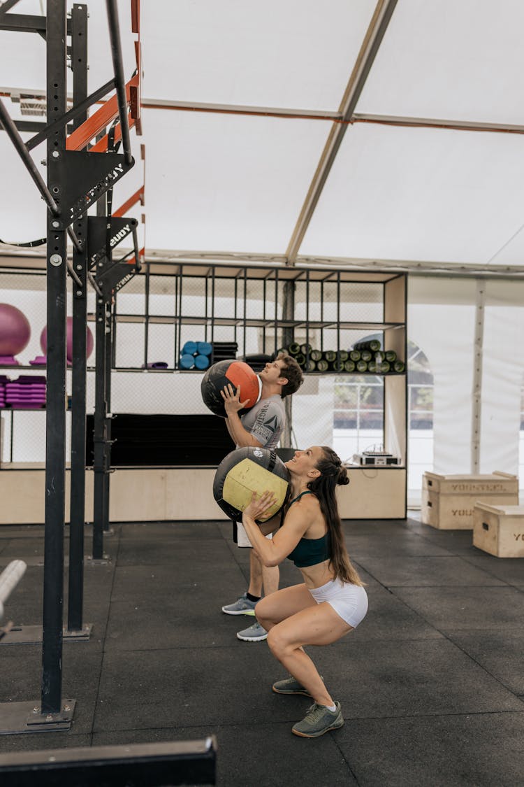 Man And Woman Lifting Medicine Balls At The Gym