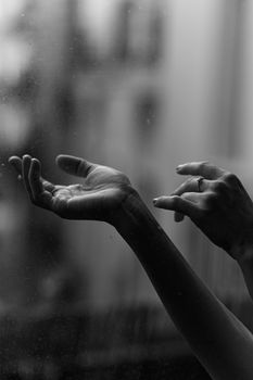 迷人的单色图像中，双手伸向模糊的雨窗