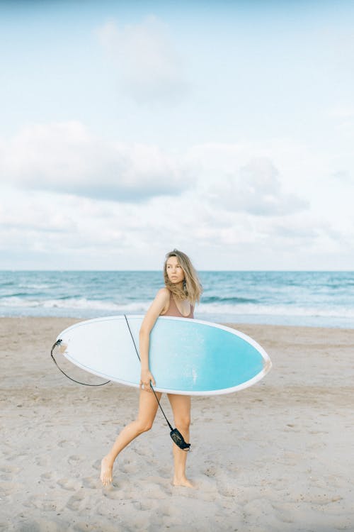 A Woman in Swimsuit Holding Blue Surfboard on Beach