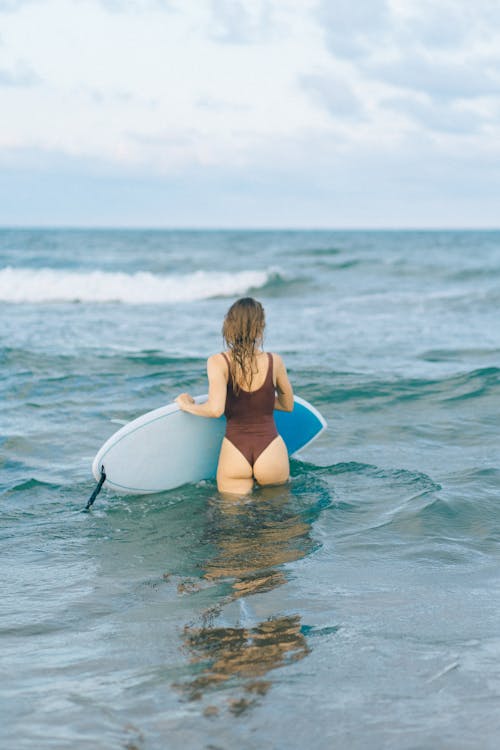 Free Woman in Blue Bikini Sitting on White Surfboard on Sea Stock Photo