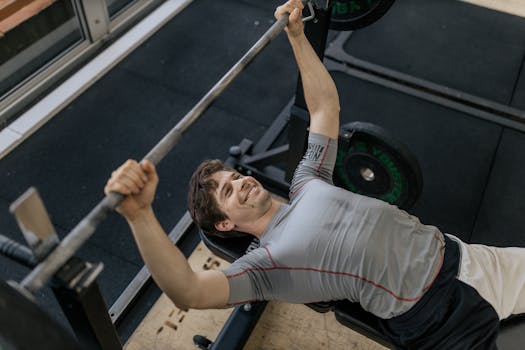 Adult man performing a barbell bench press in a modern gym, showcasing strength and fitness.