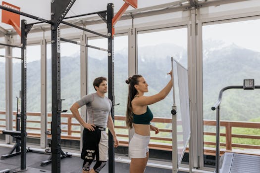 A gym coach instructs on whiteboard beside fitness equipment with mountain view.