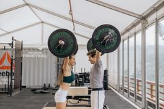 A fit man and woman lifting barbells in a modern indoor gym.