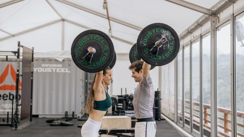 A fit man and woman lifting barbells in a modern indoor gym.