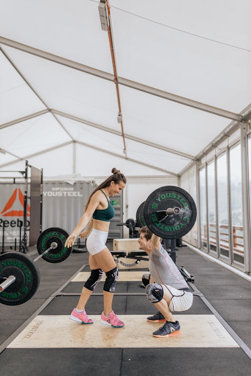 Free Man Lifting Barbell in Front of a Woman Stock Photo