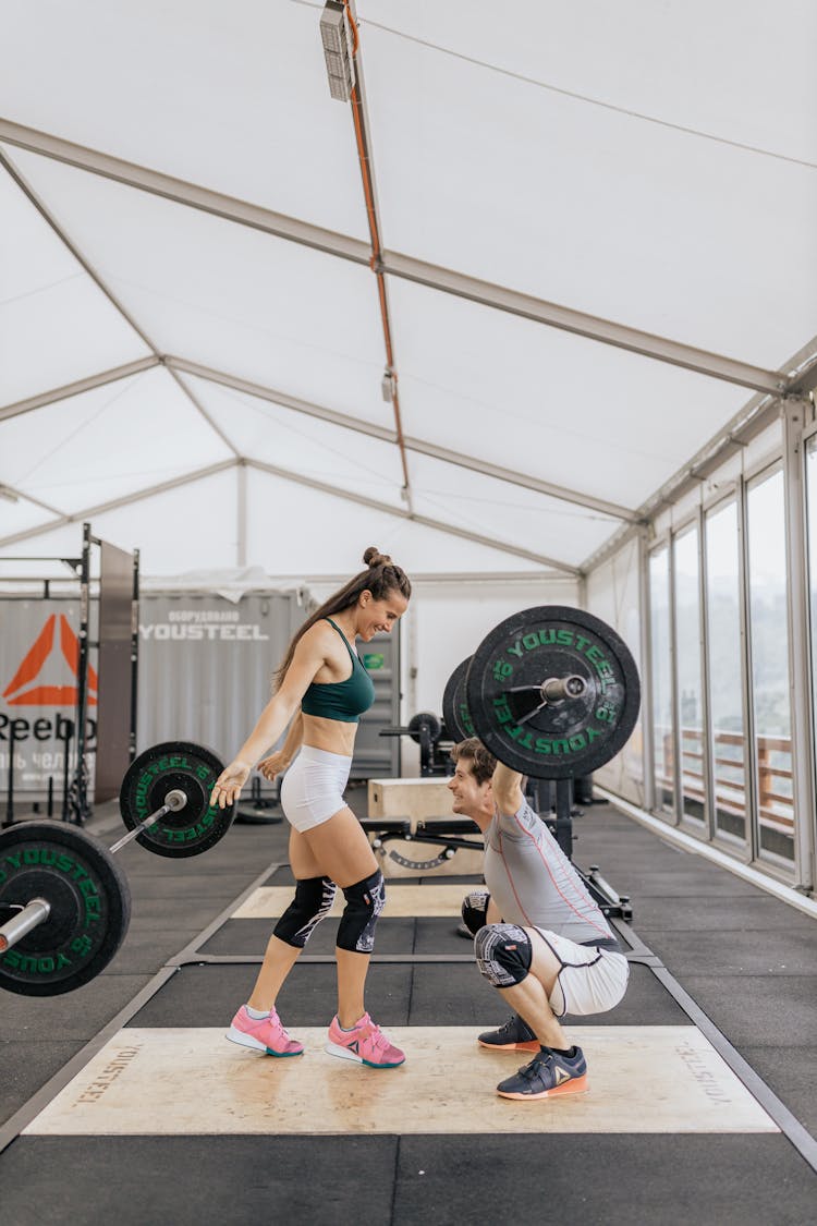 Man Lifting Barbell In Front Of A Woman