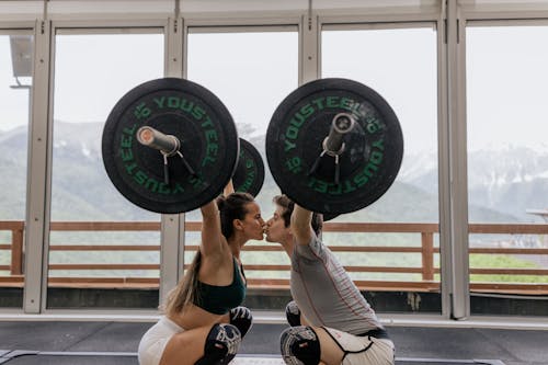 Free Couple Kissing While Lifting Barbells Stock Photo