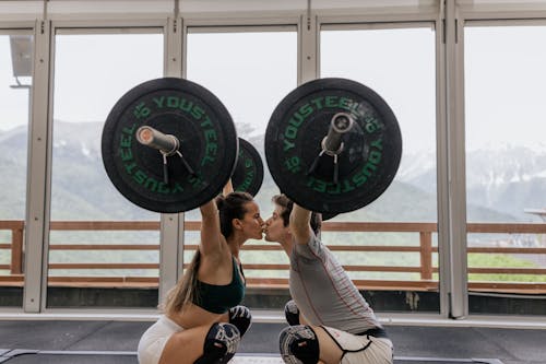 Couple Kissing While Lifting Barbells