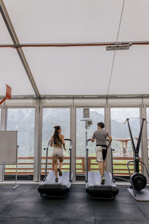 Free Back view of a couple running on treadmills in a gym with a scenic mountain view. Stock Photo