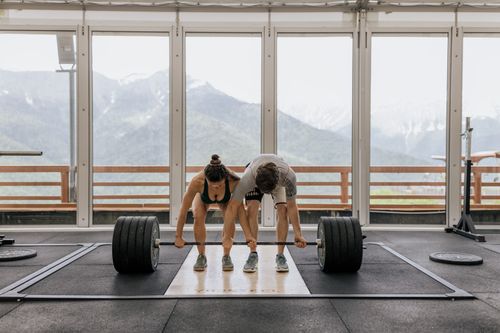 Free A couple lifting a heavy barbell together in a gym with mountain views. Stock Photo
