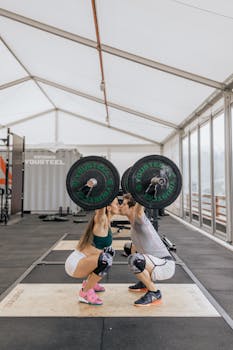 A couple in activewear shares a moment while weightlifting in an indoor gym setup.