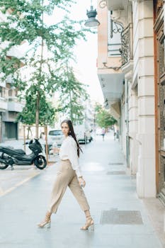 Fashionable woman in urban setting walking with confidence on a sunny sidewalk.